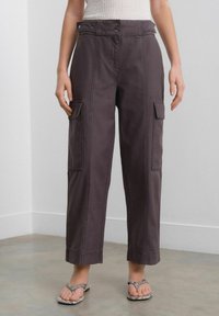 Cargo pants in dark gray fabric, featuring side pockets, a high waist with two buttons, and wide-cut legs. Textured material with seams visible.