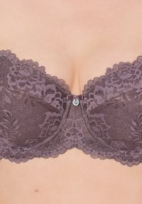 Fialová krajková podprsenka s květinovými vzory, vroubkovanými okraji a centrálním dekorativním knoflíkem. Měkká textura s pevným podporným drátkem.