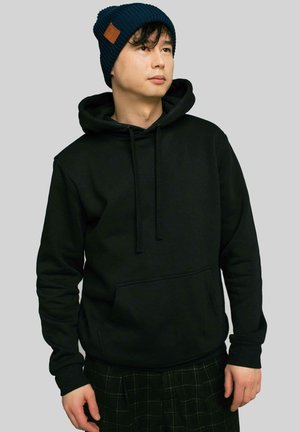 Czarna bawełniana bluza z kapturem, z kieszenią typu kangur i ściągaczami. Noszona z granatowym, prążkowanym beanie z naszywką ze skóry.