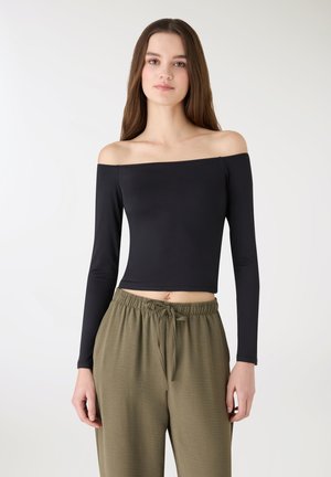 Czarna, długi rękaw, bluzka z odkrytymi ramionami, krótki fason. Gładka tekstura z dopasowanym krojem. Zestawiona z oliwkowozielonymi spodniami z troczkiem.