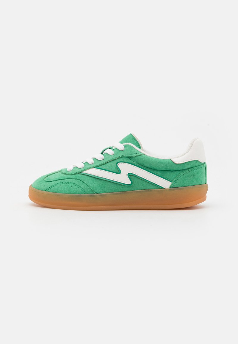 Zöld suéd sneaker fehér cikk-cakk díszítéssel, kerek orral, fehér fűzővel és világosbarna gumitalppal. Alacsony szárú kialakítással rendelkezik.