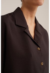 Camisa negra de botones con cuello clásico, confeccionada en tejido texturizado y con botones marrones en contraste.