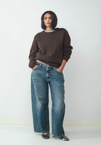Brown knitted sweater paired with light blue wide-leg jeans. Features include a round neckline and shiny black flats. Simple background.