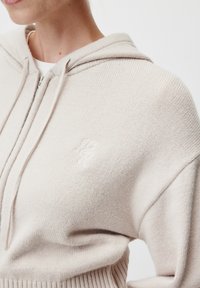 Felpa con cappuccio beige chiaro realizzata in tessuto a maglia testurizzata. Presenta una zip frontale e un logo ricamato sul petto.