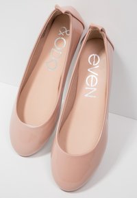 Paire de ballerines roses nude brillantes à bouts ronds et petits nœuds à l'arrière, étiquetées "even & odd" à l'intérieur.