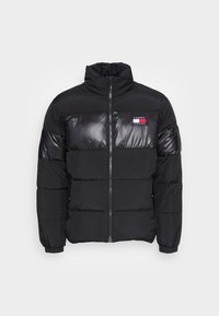 Abrigo de plumas negro con cierre de cremallera, que presenta un diseño acolchado, cuello alto y paneles brillantes; parche con el logo en el pecho.
