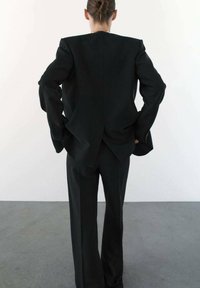 Zwart op maat gemaakt pak met een gestructureerde blazer en wijde broekspijpen. Huidige stof, minimalistisch ontwerp met lange mouwen en een rugventilatie.