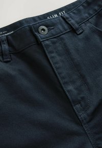 Uske slim fit tamne traperice imaju glatku teksturu, kopčanje na dugme i kontrastne šavove. Dizajnirane su s klasičnim prednjim džepovima.
