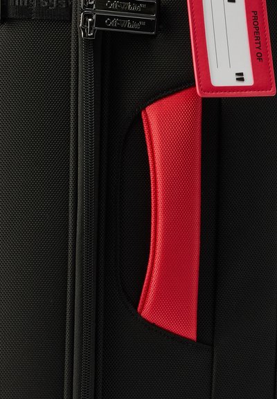 Μαύρη υφασμάτινη βαλίτσα με υφή, μαύρες τσέπες φερμουάρ με την επωνυμία Off-White, κόκκινη επενδυμένη λαβή και κόκκινη ετικέτα αποσκευών με την ένδειξη "PROPERTY OF."