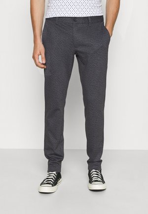 Pantalon ajusté gris foncé en tissu texturé, avec des poches latérales et une fermeture à bouton, associé à des baskets montantes noires.