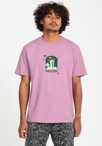 Lichtroze katoenen t-shirt met een groene grafische print met een vensterontwerp en stermotieven. Korte mouwen en een ronde hals.
