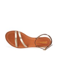 Sandale plate avec une base en cuir tan, deux brides métalliques dorées et un lien cheville marron. Comprend des détails cousus et un logo imprimé.