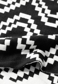 Tessuto a motivi bianco e nero con un design a zigzag. La texture appare morbida, con pieghe visibili e una finitura liscia.