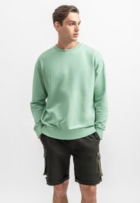 Felpa mint verde con collo rotondo realizzata in tessuto leggero, con polsini e orlo a costine, abbinata a pantaloni cargo neri.