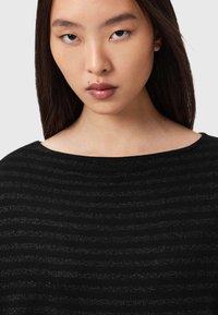 Un top negru cu dungi argintii orizontale, o decolteu larg și o textură netedă. Materialul este ușor și ușor strălucitor.