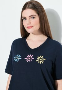 Camiseta de algodón navy con cuello en V y mangas cortas, con tres flores bordadas en azul, rosa y amarillo con acentos en negro.