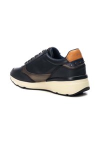 Zapatilla de cuero en azul marino oscuro y marrón con un talón en contraste color arena, cuello acolchado y detalles texturizados. Suela de color crema con dibujos en negro.