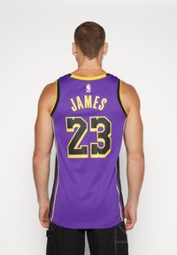 Lila baskettröja med svarta och gula accenter, med namnet "JAMES" och nummer "23" på baksidan. Mesh-material och ärmlös design.