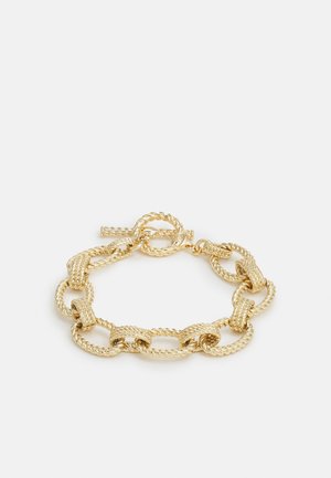 Armband met goudkleurige afwerking, voorzien van grote, getextureerde gedraaide touwschakelringen en een toggle-sluiting op een lichte achtergrond.