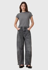 T-shirt rayé à manches courtes associé à un jean noir délavé taille haute et à jambes larges, avec des ourlets effilochés et des poches avant. Chaussures noires.