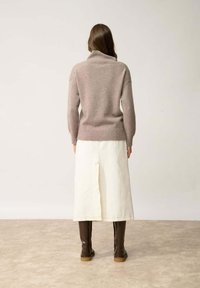 Beżowy sweter z dzianiny z wysokim kołnierzem, noszony na białej spódnicy do kostek. Całość uzupełniają brązowe kozaki sięgające za kolano.