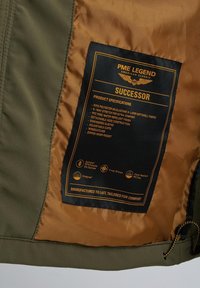 Zelena jakna od mekog materijala s smešnom unutrašnjom oblogom, s oznakom koja sadrži informacije o materijalu i uputstvima za održavanje u crnom tekstu.