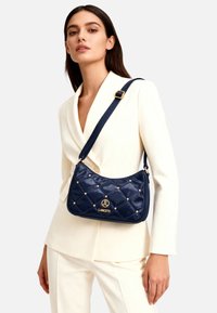 Borsa a spalla in pelle verniciata trapuntata blu navy con dettagli dorati, caratterizzata da un logo prominente e particolari borchiati.