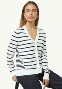 Weißer Cardigan mit marineblauen Streifen, tiefem V-Ausschnitt, vorderem Knopfverschluss und seitlichen Details. Aus weichem Strickmaterial, mit langen Ärmeln.