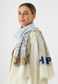 Lichte sjaal met een mix van blauw, grijs en crème kleuren, met dierlijke patronen en tekstaccenten in bruin en blauw. Afgewerkte randen.