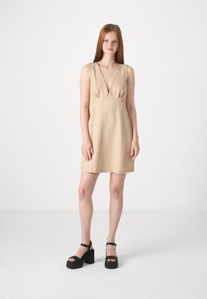Robe en lin beige avec un décolleté en V et un rassemblement sous le buste. Associée à des sandales à plateforme noires avec des brides au niveau des chevilles. Texture lisse, design simple.