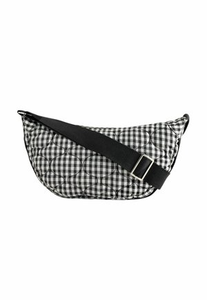 Sac bandoulière matelassé à carreaux noir et blanc avec large sangle noire réglable et boucle argentée sur fond blanc.
