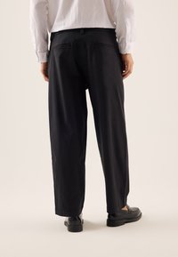 Pantaloni neri a gamba larga realizzati in tessuto liscio. Presentano una vita a media altezza e due tasche posteriori. Abbinati a scarpe nere eleganti.