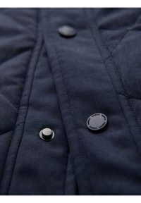 Tessuto trapuntato navy con cuciture diagonali, caratterizzato da due bottoni a pressione neri. Superficie liscia con una leggera lucentezza e senza modelli visibili.
