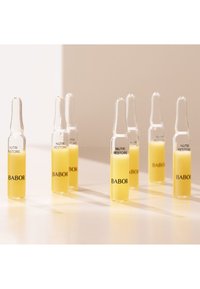 Sept petites ampoules en verre contenant un liquide jaune, étiquetées "BABOR Nutri Restore", posées sur une surface blanche avec des ombres douces.