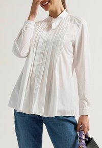 Witte shirt met een geplooide voorkant, knoopkraag en lange mouwen. Gecombineerd met blauwe spijkerbroeken en een gestreepte tas. Zachte stof, nauwsluitende pasvorm.