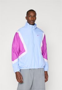 Light blue Nike jacket with purple and white accents, high collar, full-zip front, elastic waistband, and long sleeves.