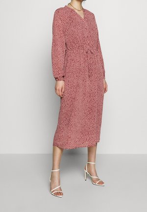 Red long-sleeve dress with white dotted pattern, V-neck, cinched waist, and flowy skirt, paired with white strappy heels.