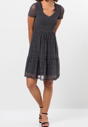 Robe noire avec des manches courtes et transparentes, décolleté en V et jupe à volants. Présente un motif texturé de lignes verticales blanches sur toute la surface.