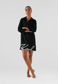 Abito camicia nero a maniche lunghe con colletto, caratterizzato da un logo bianco "K" sull'orlo e una vestibilità comoda. Texture liscia.