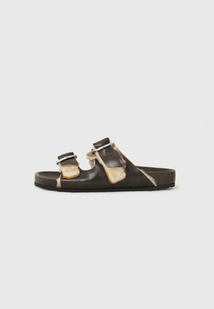 Black leather slide sandal with two adjustable straps, featuring light brown accents and a textured footbed. Flat rubber sole.