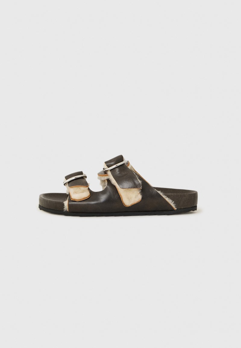 Black leather slide sandal with two adjustable straps, featuring light brown accents and a textured footbed. Flat rubber sole.