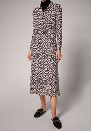 Vestido largo y estampado con líneas onduladas en negro, blanco y óxido. Fabricado en tela ligera con cuello de tipo camisero y cierre de botones en la parte delantera.