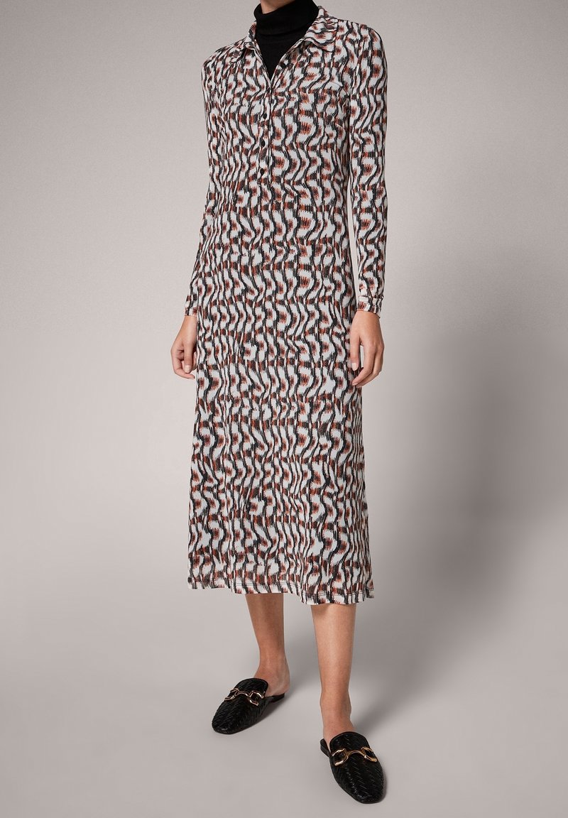 Robe longue à motifs présentant des lignes ondulées en noir, blanc et rouille. Fabriquée en tissu léger, avec un col et un devant boutonné.