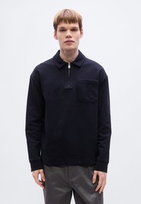 Ναυτικό φλις μπλουζάκι με γιακά, μπροστινό φερμουάρ στο μισό μήκος και τσέπη με πατς. Διαθέτει μακριά μανίκια και άνετη εφαρμογή. Ομαλή υφή.