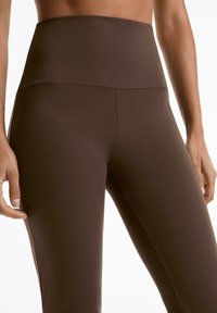 Blogin korkeavyötäröiset ruskeat leggingsit, joissa on sileä ja joustavaa kangasta, istuva muotoilu, korostetut saumat ja minimalistinen esteettisyys.