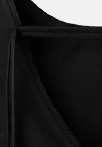 Primer plano de tela negra con costuras visibles y detalles de costura en el borde o cuello de una prenda.