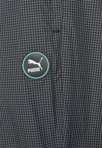 Svart och vit rutigt tyg med en slät textur. Har en rund svart Puma-logotyp med turkosa detaljer.