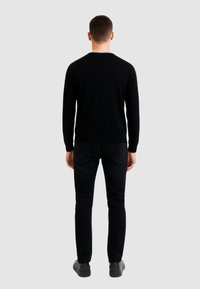 Zwarte gebreide trui met lange mouwen, ronde hals, gecombineerd met zwarte broek. Gladde textuur, aansluitende pasvorm en minimale details.