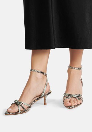 Sandały na cienkim obcasie z paskami, z plecionym wzorem w zielono-czarny wzór wężowy. Otwarty nosek z kokardką z przodu.