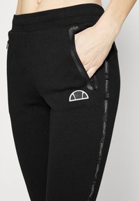 Schwarze Sweatpants mit einem gerippten Bund, Seitentaschen und einem kontrastierenden Logo an der Hüfte. Mit einem strukturierten Seitenstreifen und Branding.